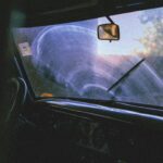 Home Moody interior view of a vintage car through a foggy windshield, highlighting steering wheel and rear view mirror.
