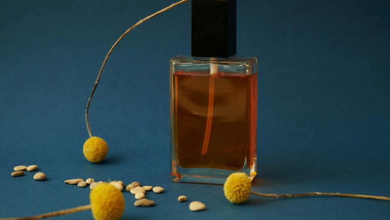 Elegant perfume bottle with yellow flowers and seeds on a blue background. Perfect for product mockups.