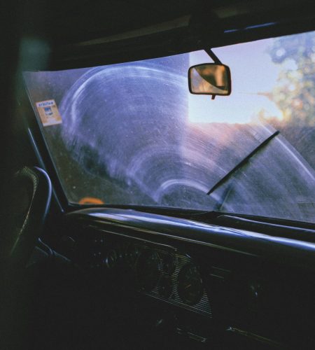 Moody interior view of a vintage car through a foggy windshield, highlighting steering wheel and rear view mirror.